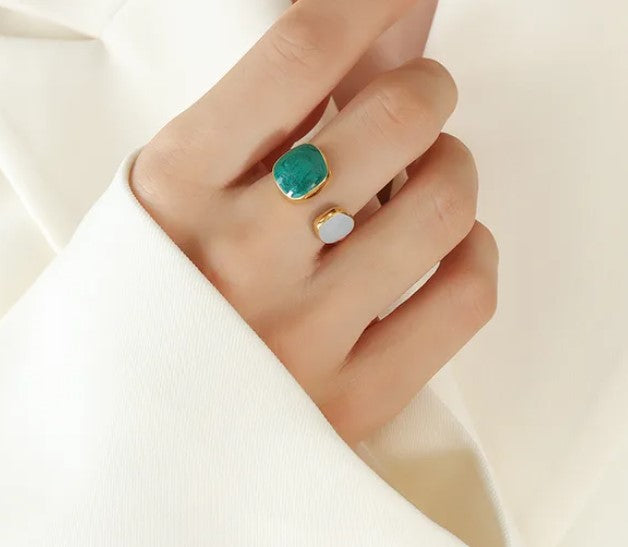 Hand wearing two rings with a green gemstone and gold band on a light background