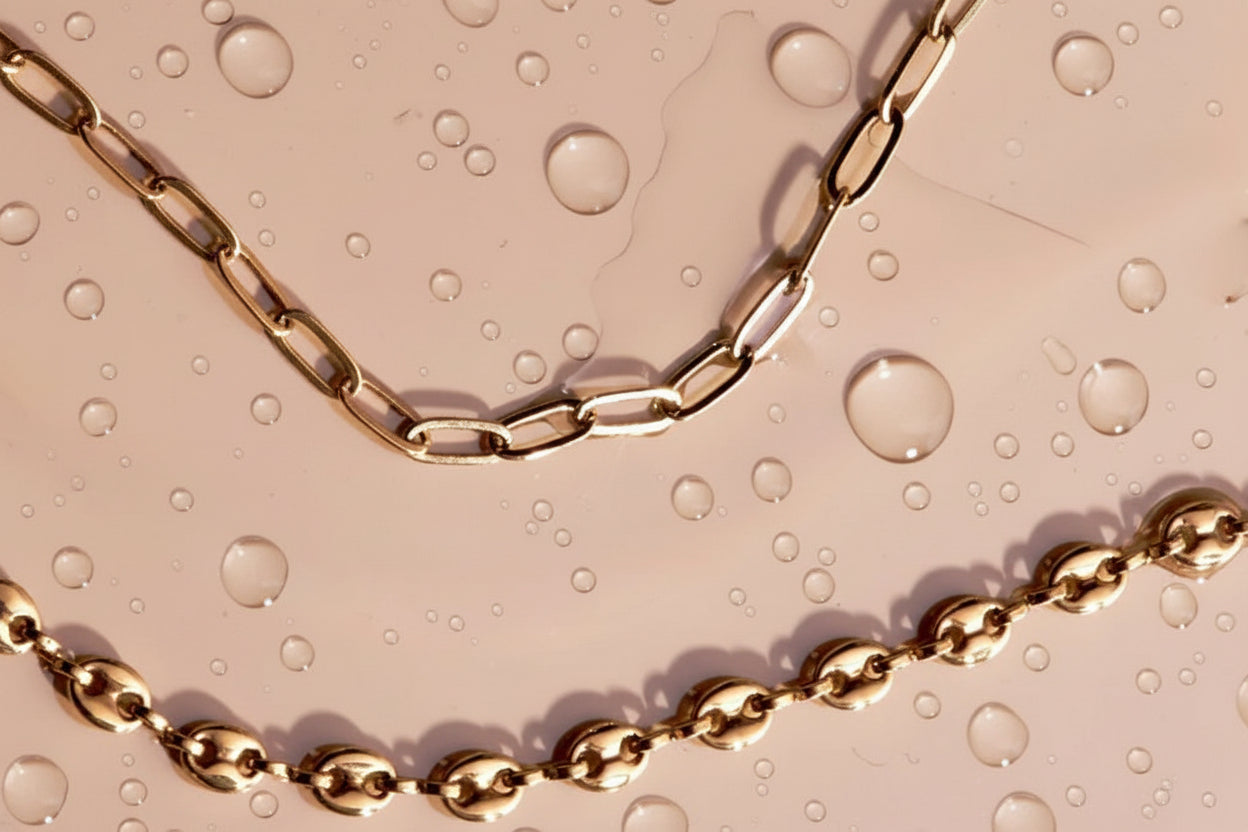 Two gold chains on a beige surface with water droplets.